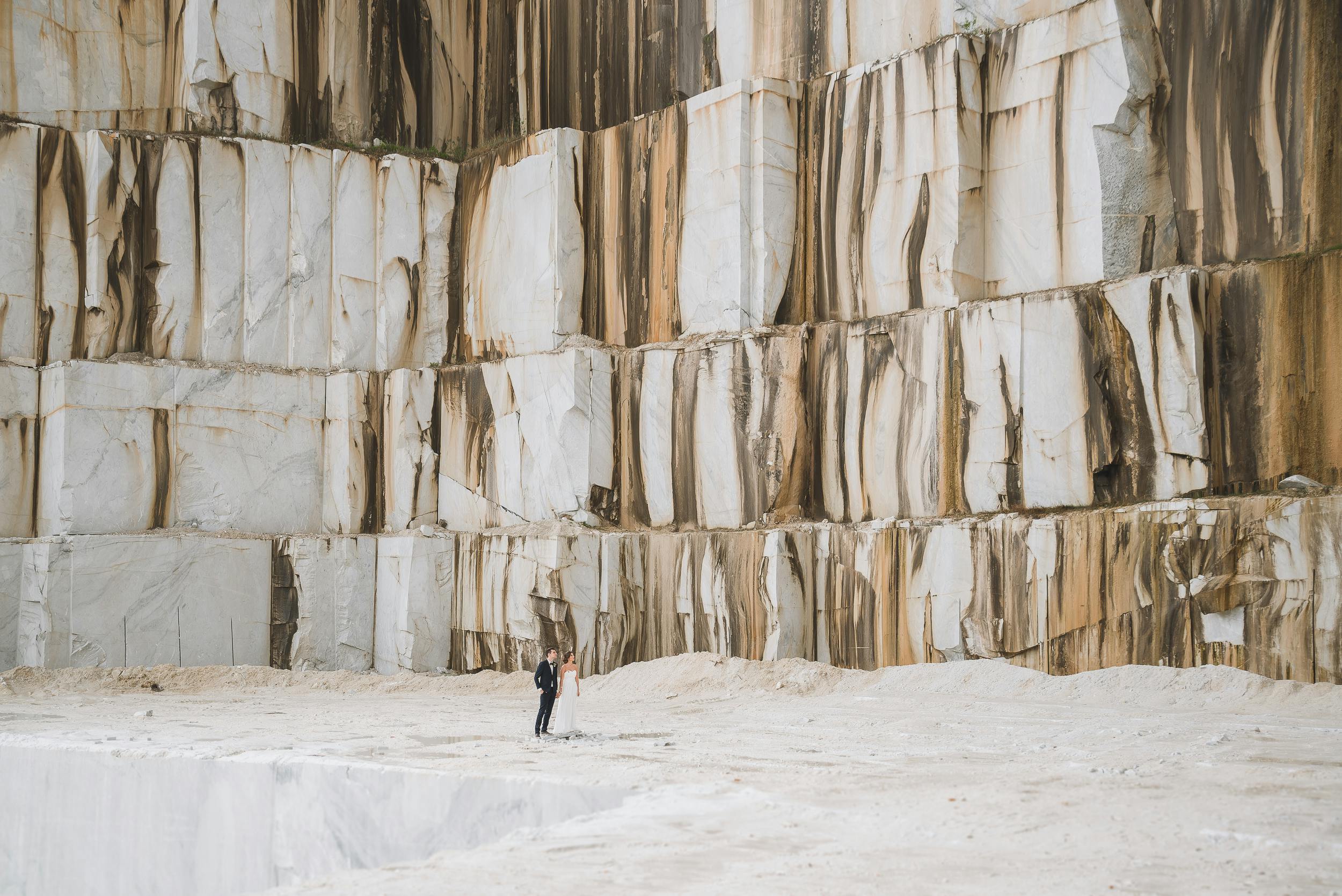 A couple stands in awe at a vast marble quarry, showcasing impressive stone formations.
